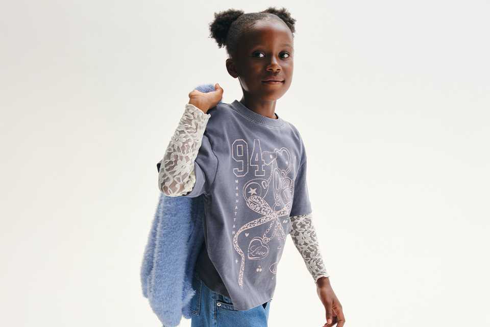 A girl wearing a long denim skirt, with a t-shirt, and long lace top underneath.