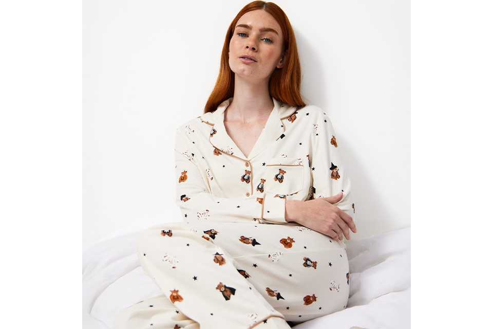 erson wearing white printed pyjamas sitting on a bed, featured in the Tu Clothing nightwear guide.