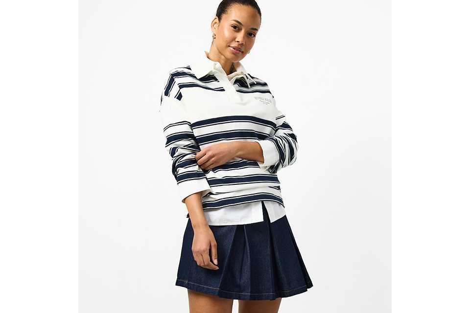 A woman wearing a stripey long-sleeve top, with a denim mini skirt, and loafers with socks.