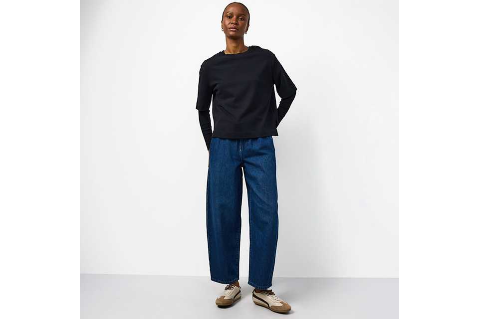 women wearing blue barrel leg jeans, with a black basic long sleeve top and trainers.