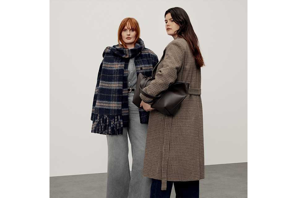 Two women wearing coats, one coat has a scarf attached.
