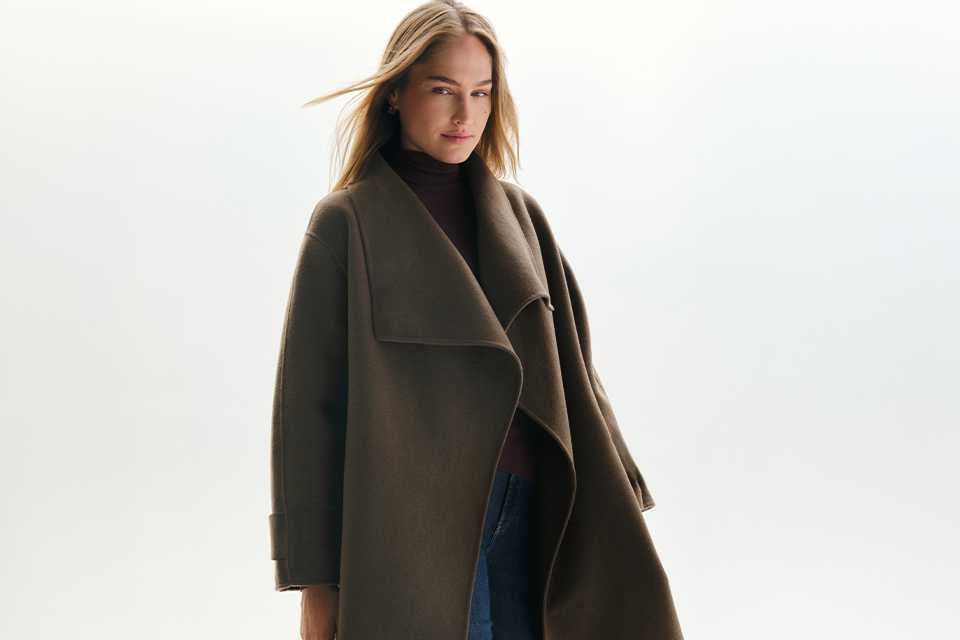 A woman wearing a roll neck jumper with jeans with a coat over the top.