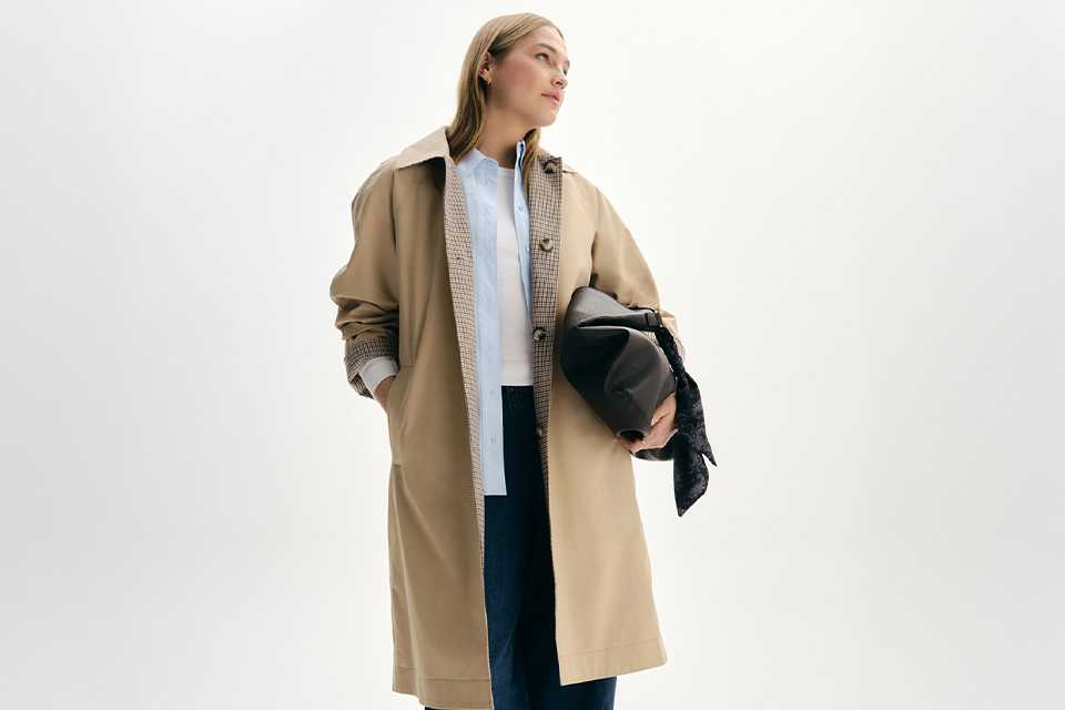 A woman wearing a white top with blue shirt, paired with barrel-leg trousers, and then a reversible trench coat.