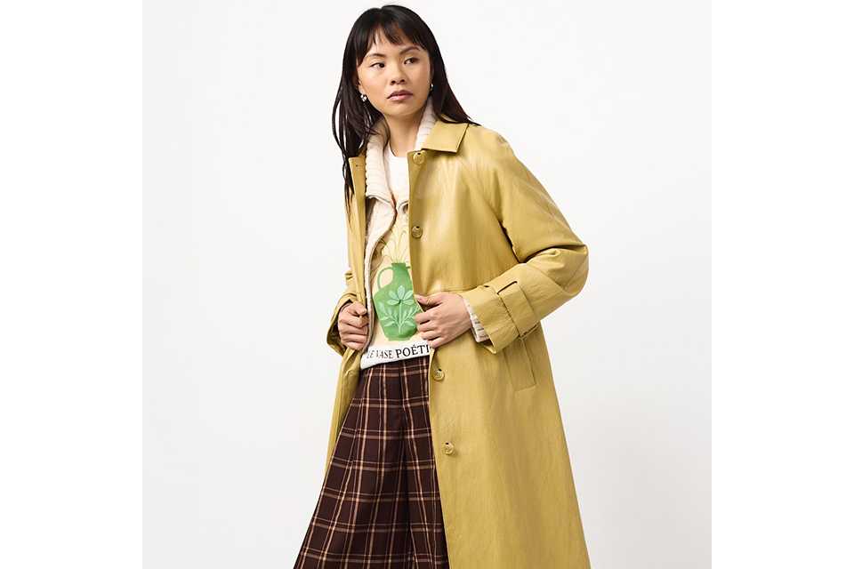 Woman wearing an ochre PU coat, with wide leg check trousers, brown trouzers and a top.