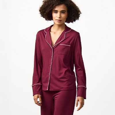 Women's satin pyjama set in burgundy with long-sleeve button-up top and matching trousers, comfortable coordinated nightwear.