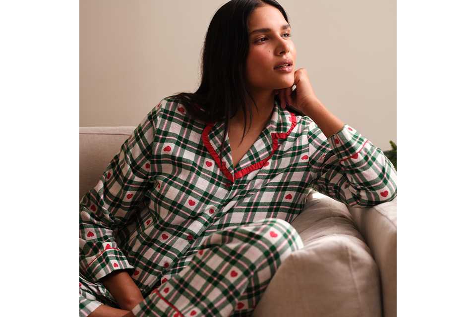 Person relaxing in traditional tartan check Christmas pyjamas with red and green festive styling.