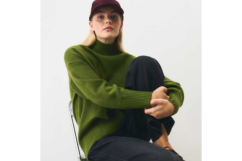 Close-up of a child wearing a brown graphic sweatshirt featuring playful dinosaur illustrations and bold cream lettering, photographed indoors against a neutral tiled background.