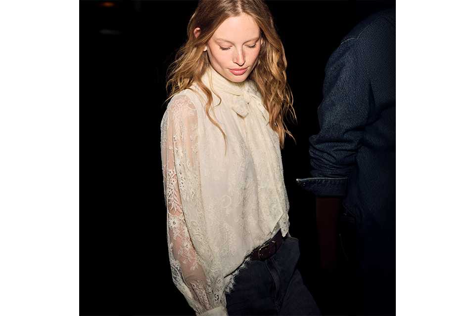 Cream lace high-neck blouse with tie-neck detail and sheer long sleeves, styled with blue denim jeans for an elegant casual outfit.