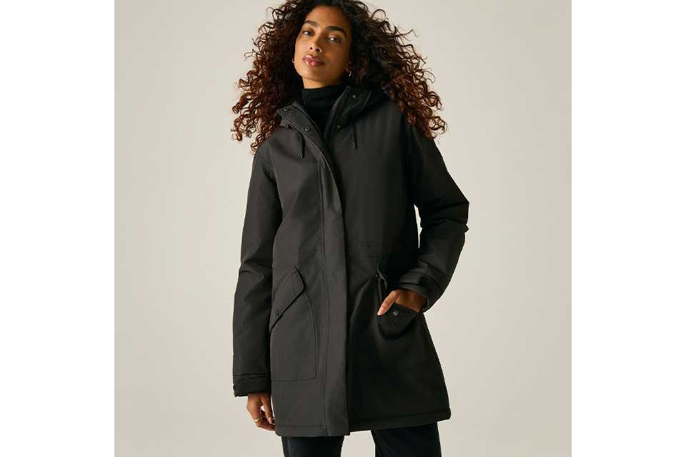 Black hooded waterproof parka jacket worn over a black turtleneck, featuring a full front zip closure, adjustable hood, and utility pockets in a minimalist studio setting.