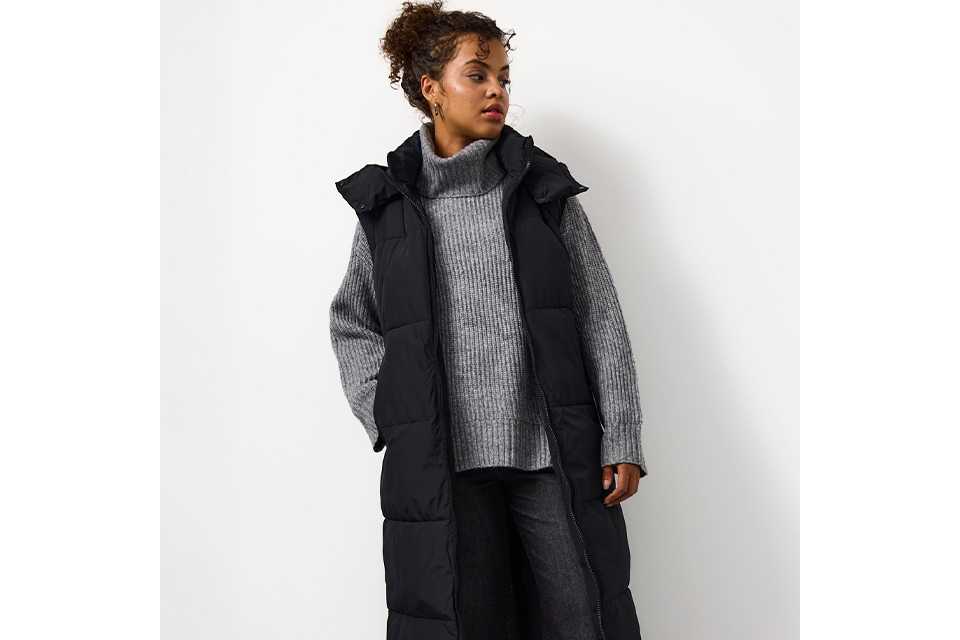 A woman wearing a grey jumper, with dark jeans and a black longline padded gilet.