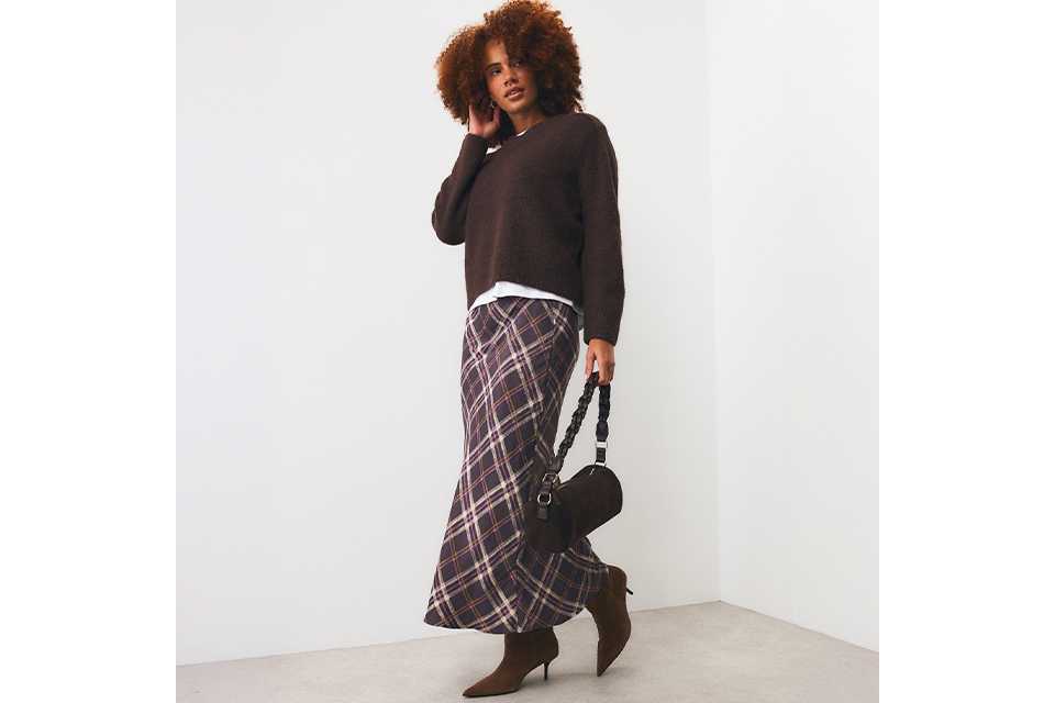 Woman wearing brown jumper and check midi skirt with brown kitten heeled boots.