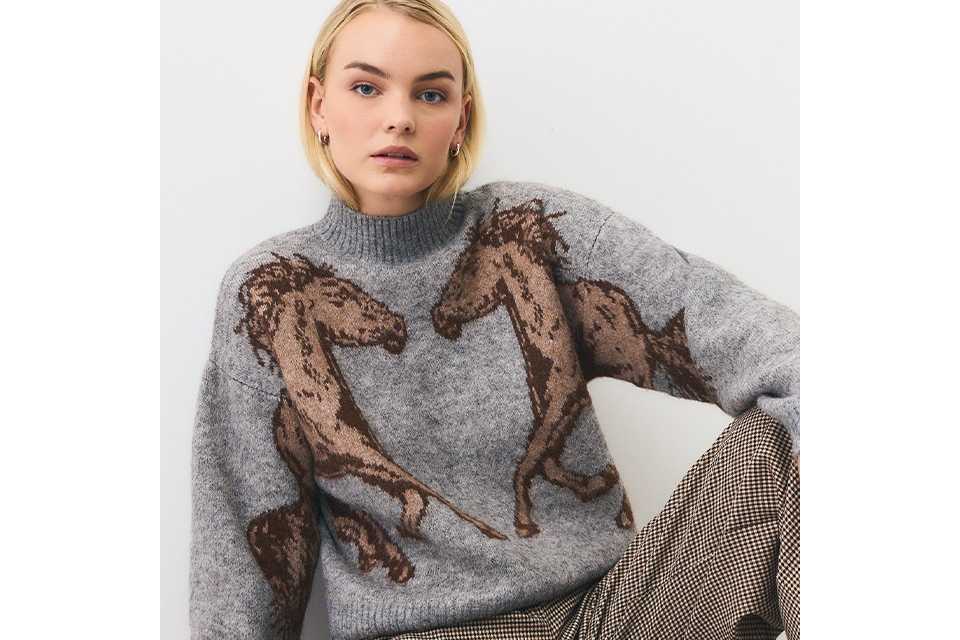 A woman wearing a grey jumper with brown horses on it.