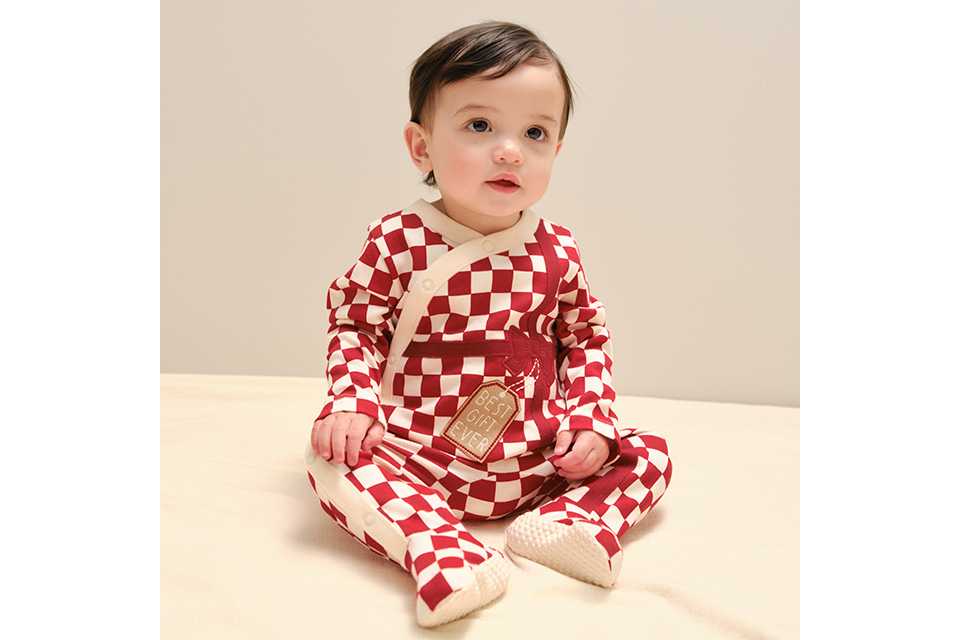 A baby wearing a red and white checkered sleepsuit with a 'best gift ever' motif.