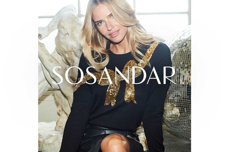 A woman wearing a black jumper with a gold bow.