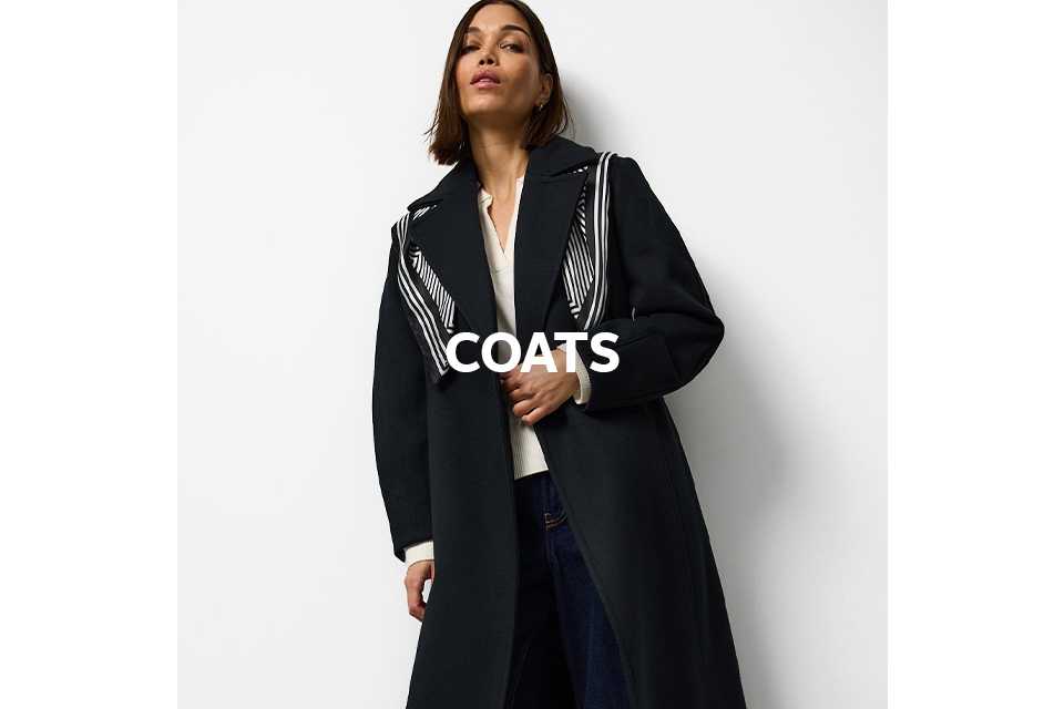 A woman wearing a full length black coat with a black and white scarf accessoring it.