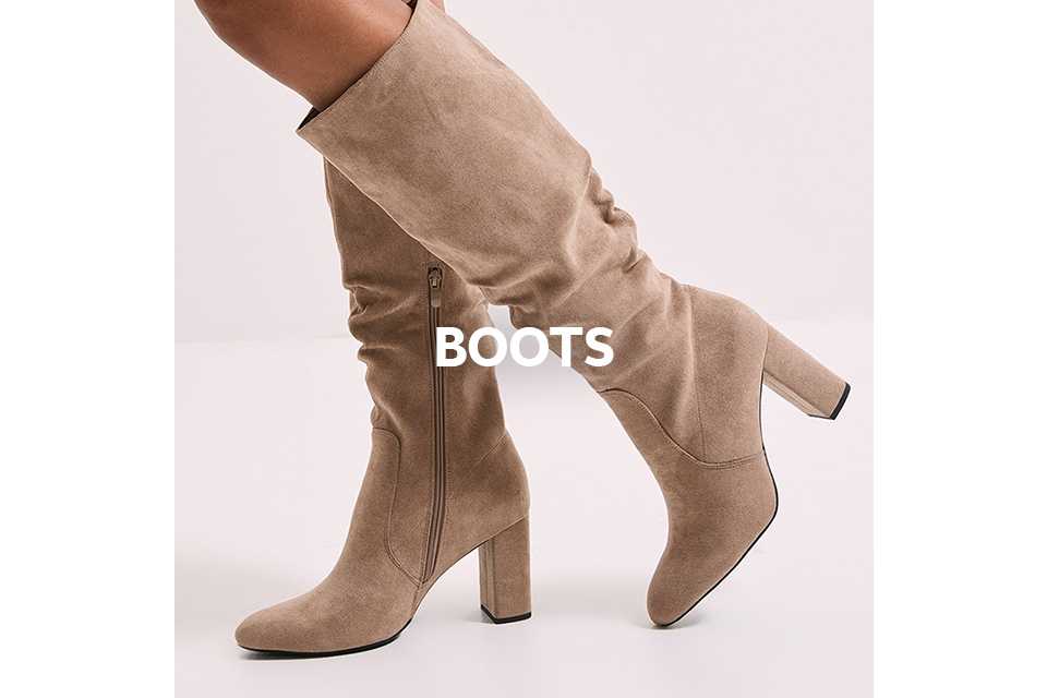 A woman wearing taupe ruched knee high boots with a heel.