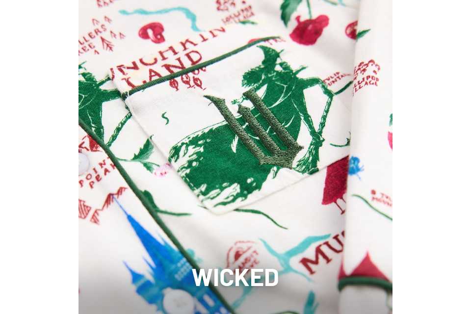 Close-up of fabric featuring green illustrations and red text inspired by the musical Wicked, with scattered decorative elements.