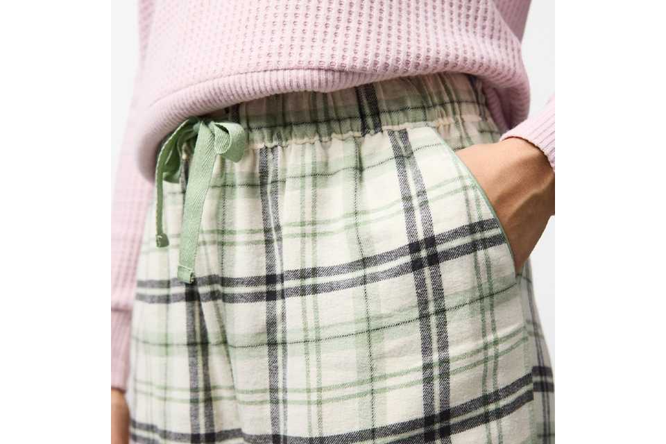 Woman wearing check pyjamas bottoms with a light pink top.