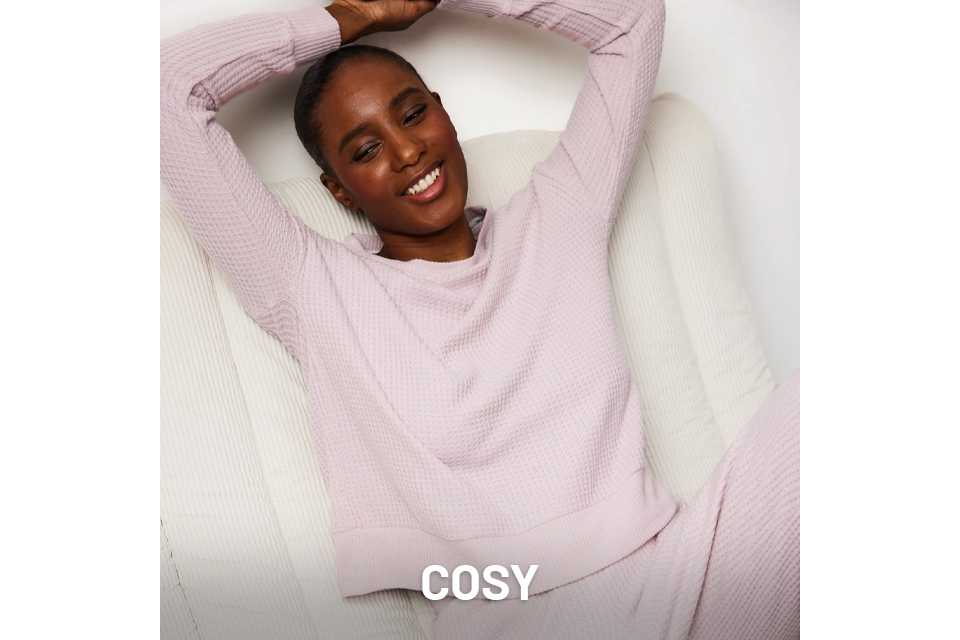 Person reclining on a white textured chair, wearing a light lavender waffle-knit loungewear set with a long-sleeve top and matching pants.