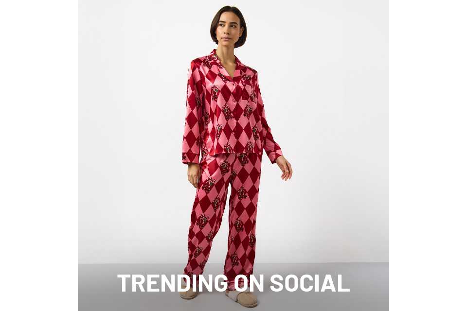 Person wearing a pink and red satin pajama set with a diamond pattern and decorative motifs, paired with beige slippers, standing against a plain white background.