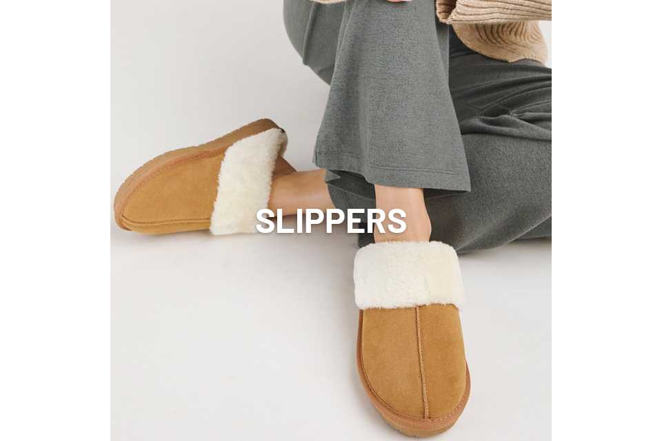 A women sat down, wearing grey bottoms and tan slippers with white faux fur.