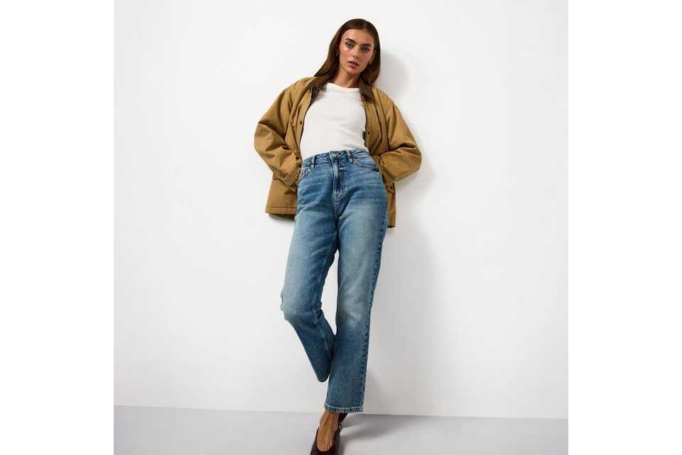 Woman wearing straight leg jeans a white t shirt and tan jacket.