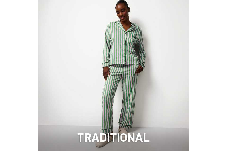 Person standing against a white background wearing a green and white vertically striped pajama set with a button-up top and matching pants, paired with light-colored slippers.