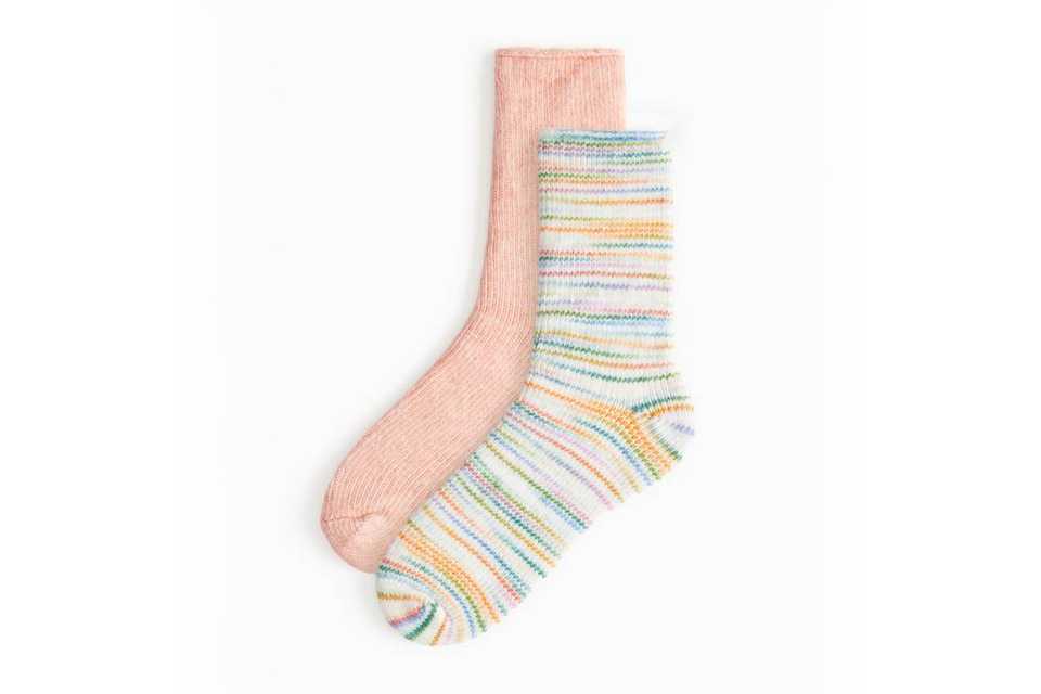 Pair of cosy winter socks, one in solid pink and the other in white with colorful stripes.