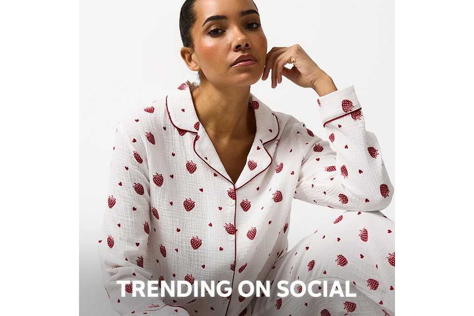 Person wearing a pink and red satin pajama set with a diamond pattern and decorative motifs, paired with beige slippers, standing against a plain white background.