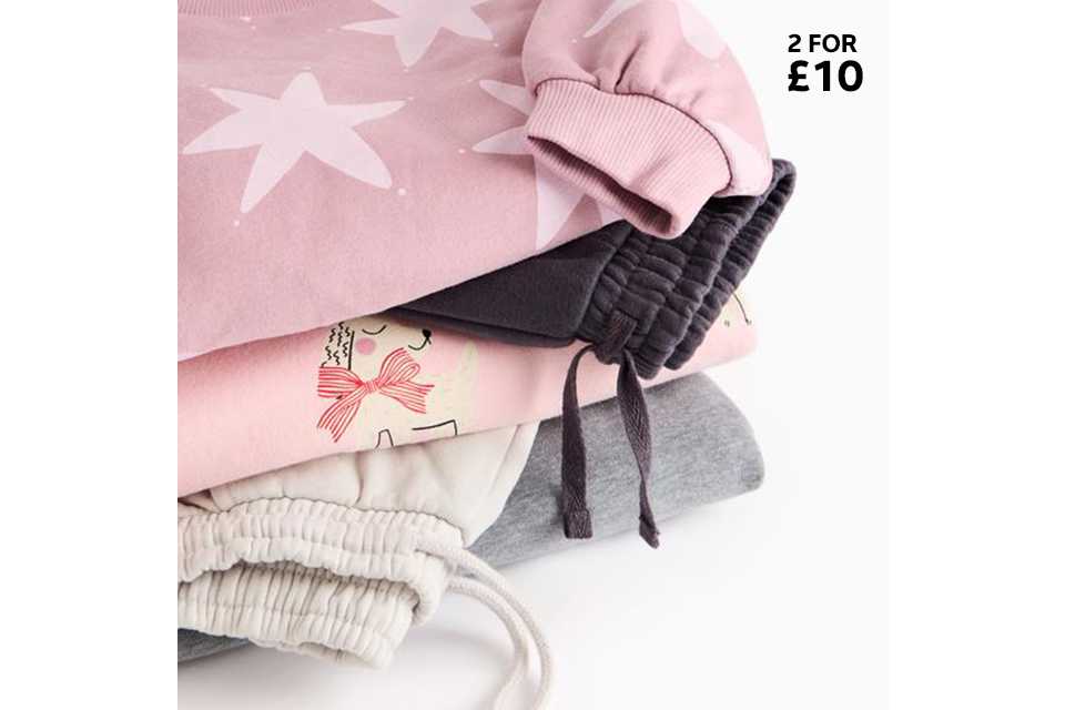 Stack of pastel joggers and sweatshirts, including pink, grey, and star‑print pieces.