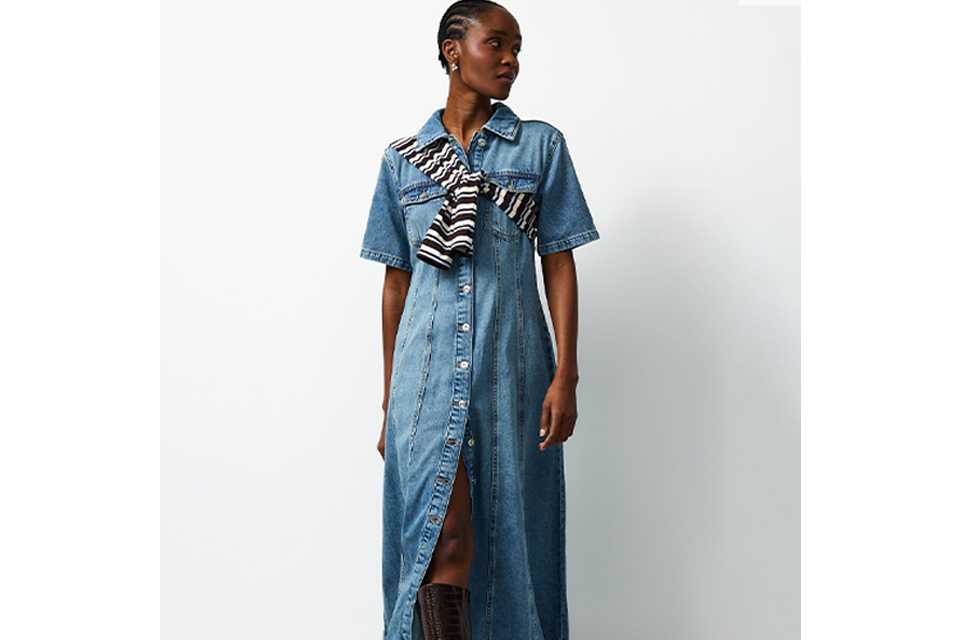 Person wearing a black long-sleeve ribbed top paired with a high-waisted black denim midi skirt featuring a front slit, styled with white sneakers.