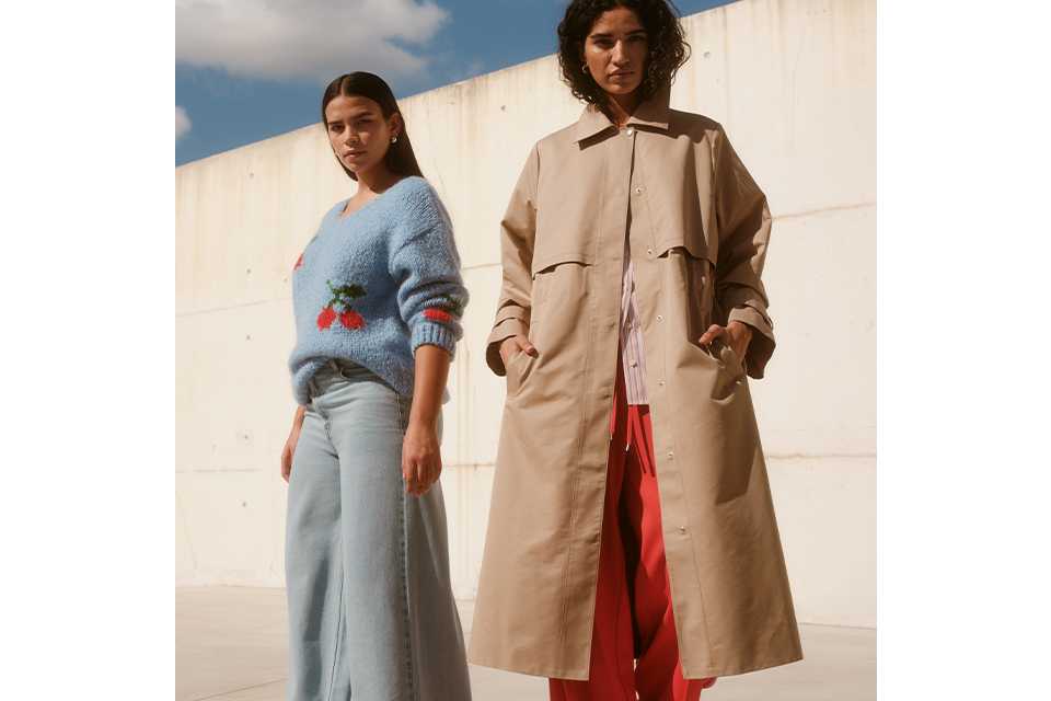 Two people wearing spring denim outfits: one in a blue embroidered sweater with wide‑leg jeans, and one in a beige trench coat layered over a red dress.