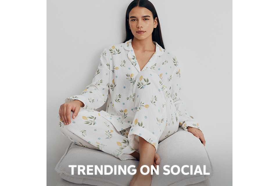 Person wearing a pink and red satin pajama set with a diamond pattern and decorative motifs, paired with beige slippers, standing against a plain white background.