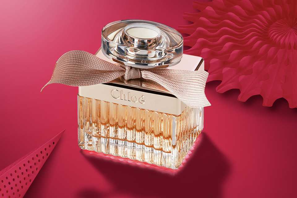 Chloé Eau de Parfum bottle with signature ribbon, styled on a pink background for luxury fragrance gifting.