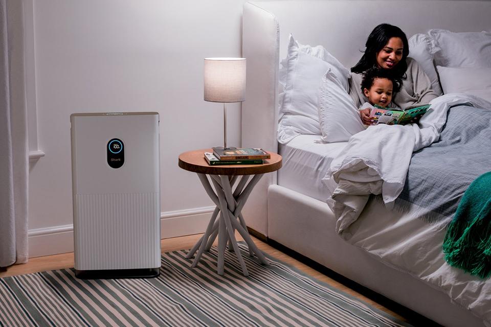 A mother reading a bedtime story to her son with a Shark 6 fan air purifier next to a bedside table.
