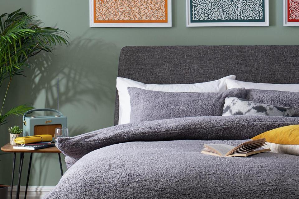 Green bedroom with grey fabric bed and wall art.