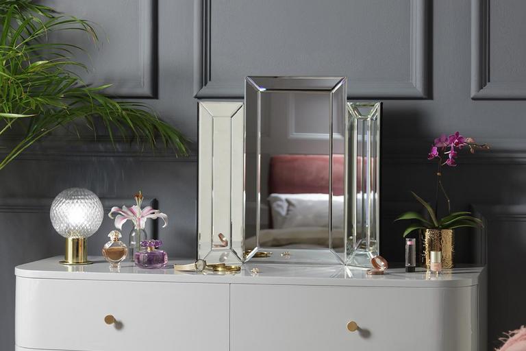 Grey chest of drawers with small mirror and perfumes on top.