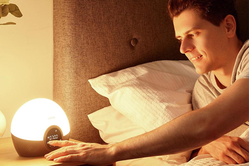 Man in bed setting his light up smart alarm clock.