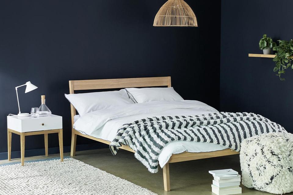 Dark blue bedroom with wooden bed frame and white bedside table.
