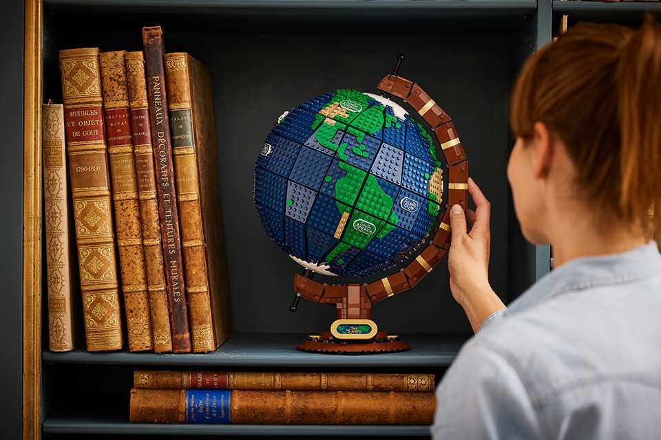 A woman places the LEGO ideas the globe onto a book shelf.
