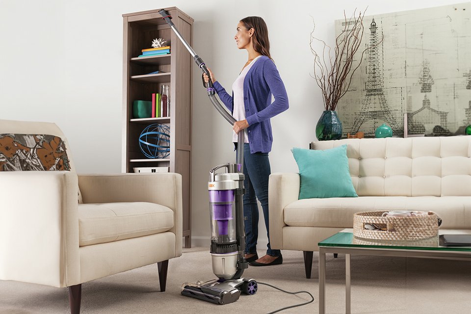 A woman cleaning the bookshelf with a Vax Air Stretch Max Pet corded upright vacuum cleaner.