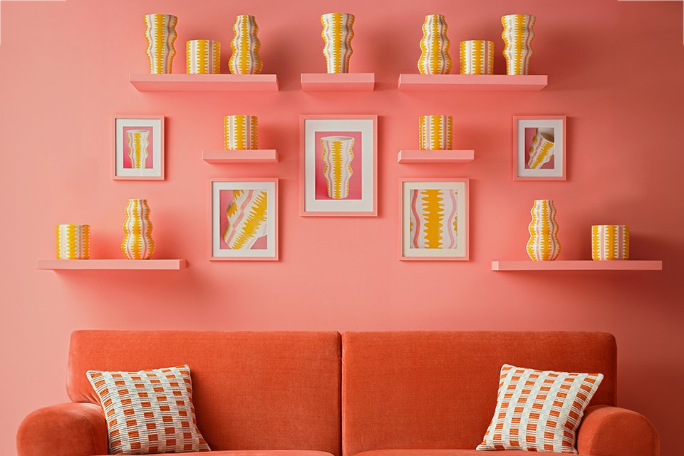 A Habitat pink sofa in front of a bright wall with vases and photo frames.