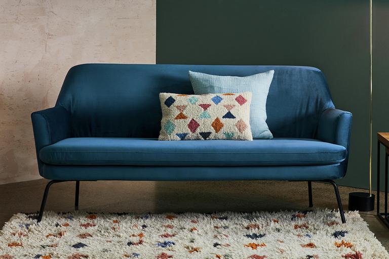 Modern blue sofa, with matching geometric patterned, fluffy rug and cushion.
