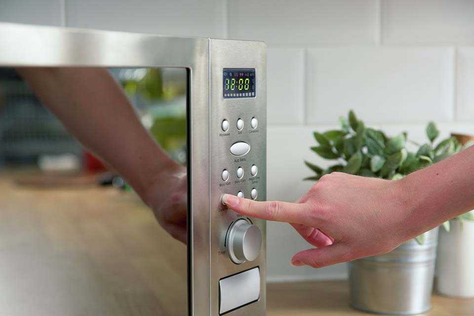 A close up image of a woman's hand using a metallic combination microwave by Russell Hobbs.