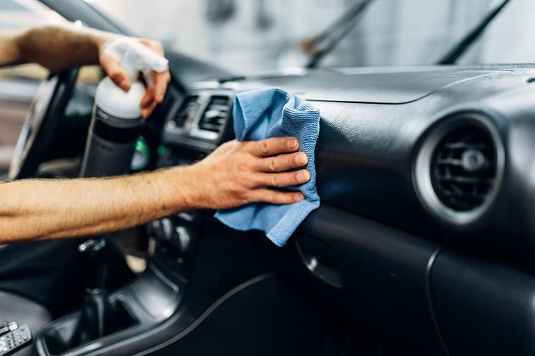 A man cleaning the car dashboard with a cleaner and blue cloth.