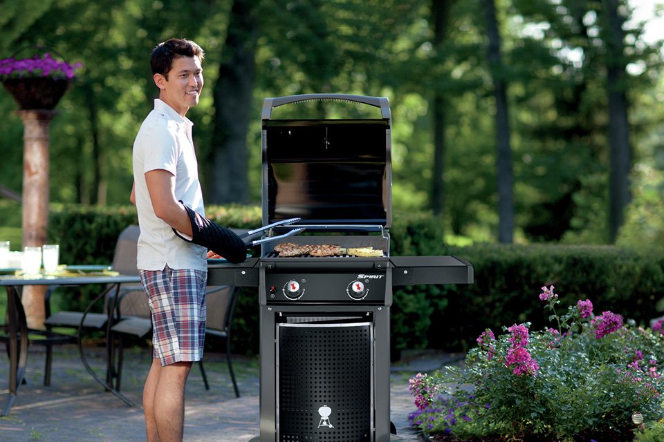 A man grilling food on a BBQ in a garden.