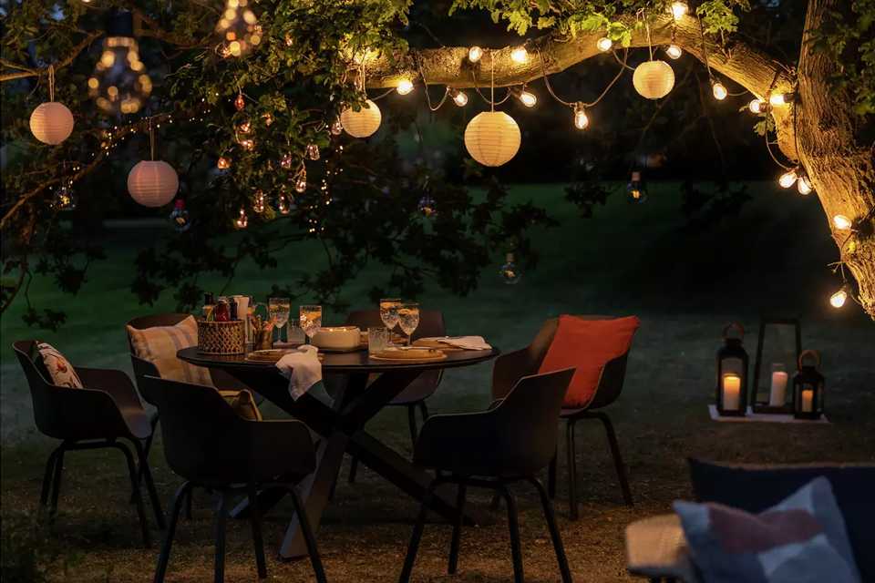 Outdoor string lights and lanterns over a Habitat Aegaen 6 seater metal patio set in grey set up for a party. 