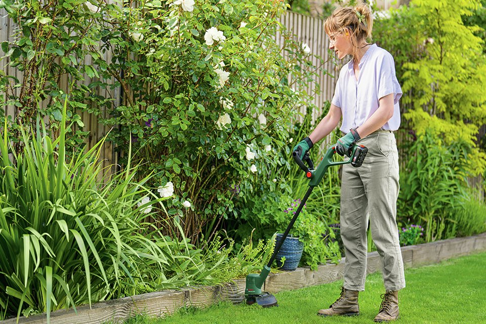 A woman using Bosch 32cm Cordless Rotary Lawnmower and Grass Trimmer. 