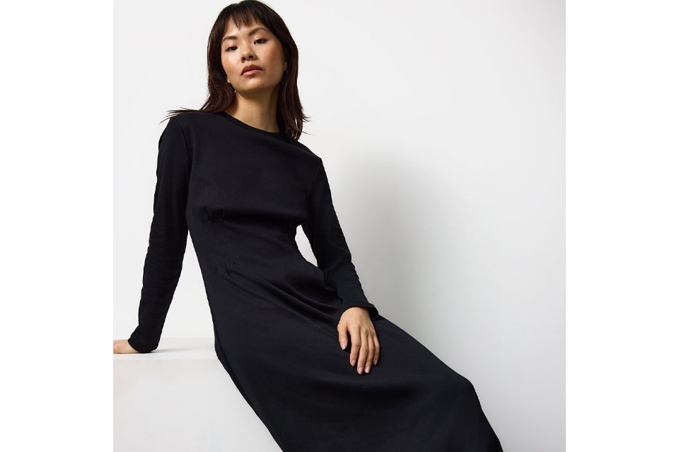 Dark green paisley mini dress with long sheer sleeves, tie‑waist detail and tiered ruffle hem, styled against a warm neutral background. 