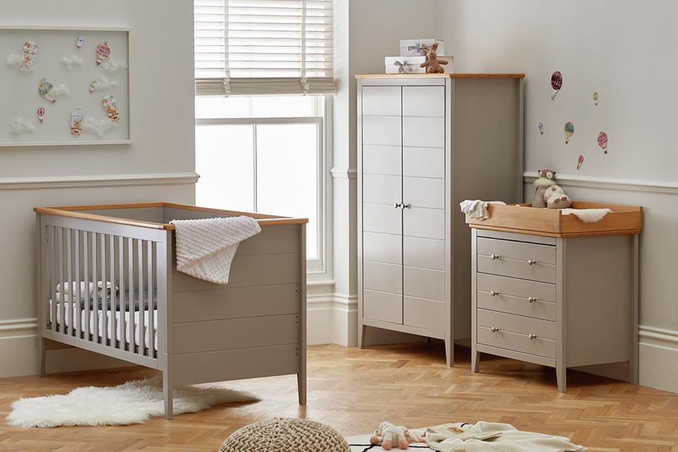 A cot bed, a wardrobe and a chest of drawers next to a window with blinds.